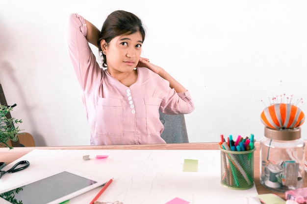 Jeune designer se sent mal à l'aise assis dans une chaise de bureau femme massant son dos souffrant d'inconfort douleur douleur mauvaise posture due à un long travail sédentaire et au concept de maux de dos inférieurs