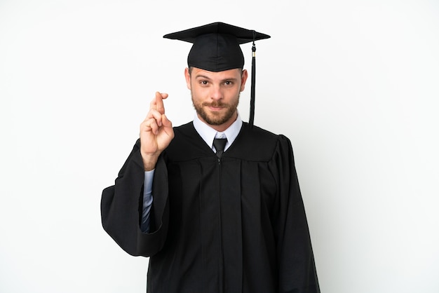 Jeune diplômé brésilien d'université isolé sur fond blanc avec les doigts croisés et souhaitant le meilleur