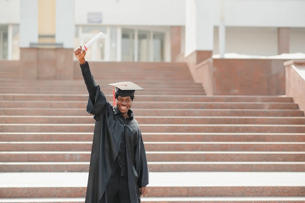 Jeune diplômé de sexe masculin africain debout devant le bâtiment de l'université