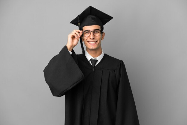 Jeune diplômé universitaire argentin isolé sur fond gris avec des lunettes et heureux