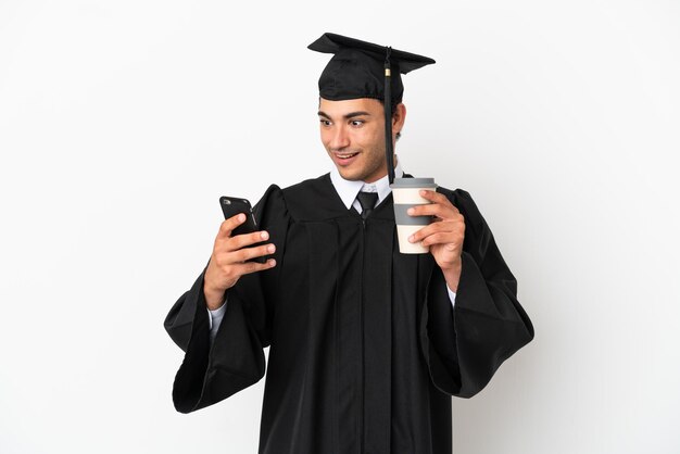 Jeune diplômé universitaire sur fond blanc isolé tenant du café à emporter et un mobile