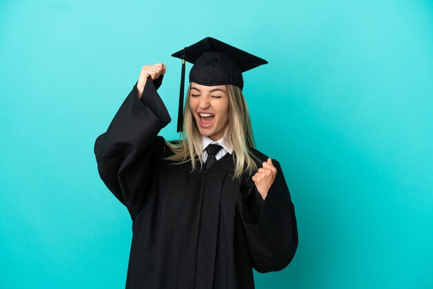 Jeune diplômé universitaire sur fond bleu isolé célébrant une victoire