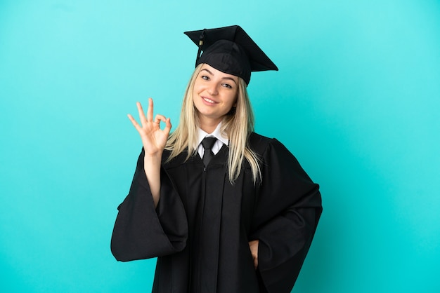 Jeune diplômé universitaire sur fond bleu isolé montrant signe ok avec les doigts