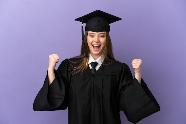 Jeune diplômé universitaire sur fond violet isolé célébrant une victoire en position de vainqueur