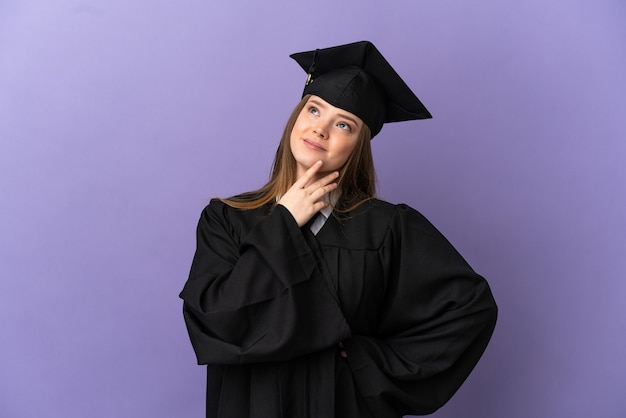 Jeune diplômé universitaire sur fond violet isolé en levant tout en souriant