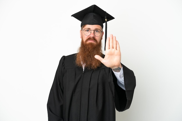 Jeune diplômé universitaire homme rougeâtre isolé sur fond blanc faisant un geste d'arrêt