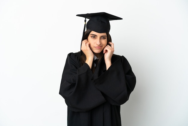 Jeune diplômé universitaire isolé sur fond blanc frustré et couvrant les oreilles