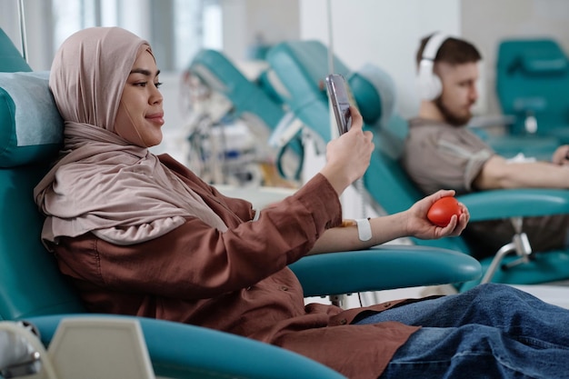 Une jeune donneuse de sang en hijab se fait un selfie dans un fauteuil médical