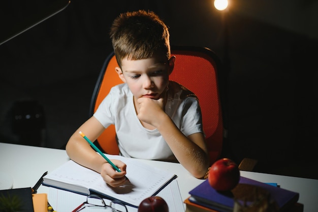 Jeune écolier adolescent à la table à faire ses devoirs dans la pièce sombre