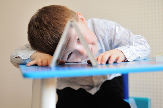 Jeune écolier jouant avec des livres et souriant alors qu'il est assis à son bureau en classe