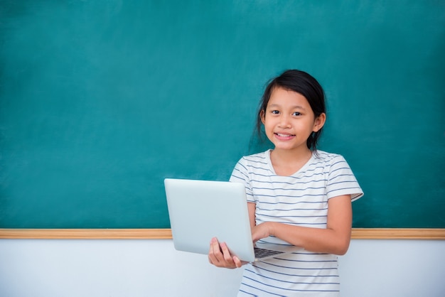 Jeune, écolière asiatique, tenue, ordinateur portable, et, sourires, devant, tableau