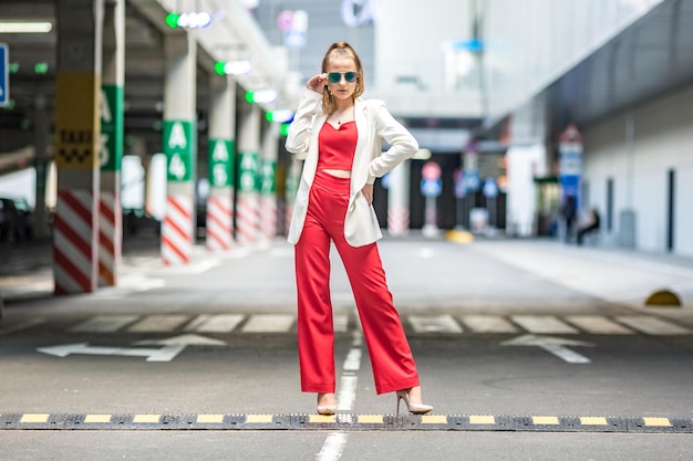 Jeune écolière blonde dans un costume rouge et une veste blanche posant dans le parking