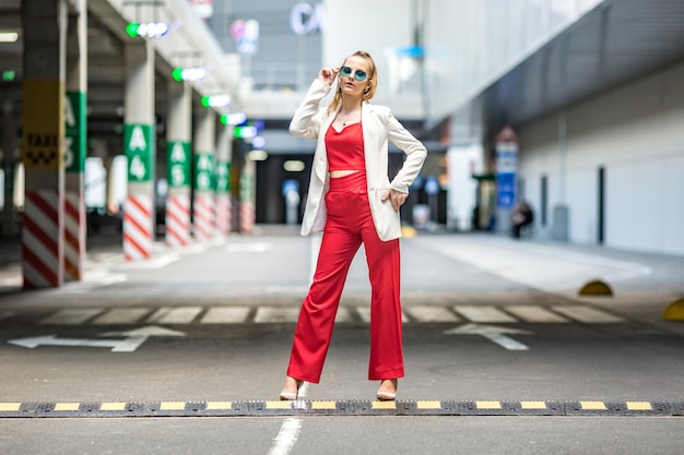 Jeune écolière blonde dans un costume rouge et une veste blanche posant dans le parking