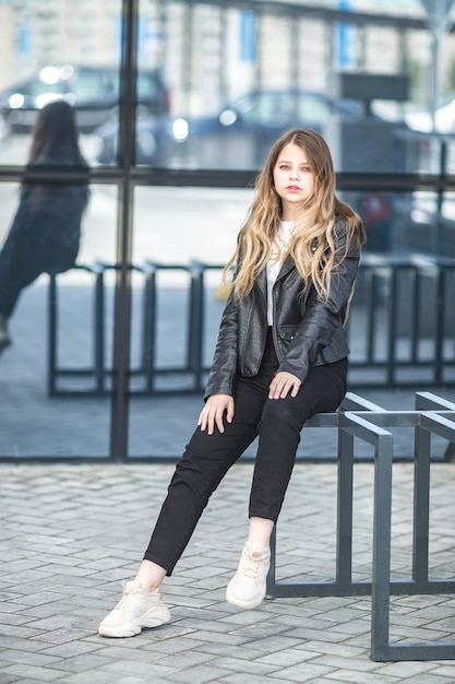 Jeune écolière en blouson de cuir noir posant dans le parking