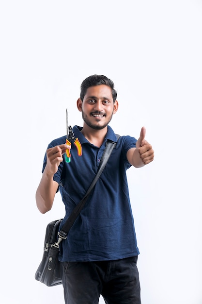 Jeune électricien indien tenant des outils à la main et debout sur fond blanc.