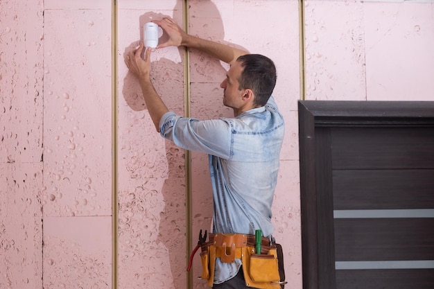 Jeune électricien installant une alarme de sécurité sur le mur.