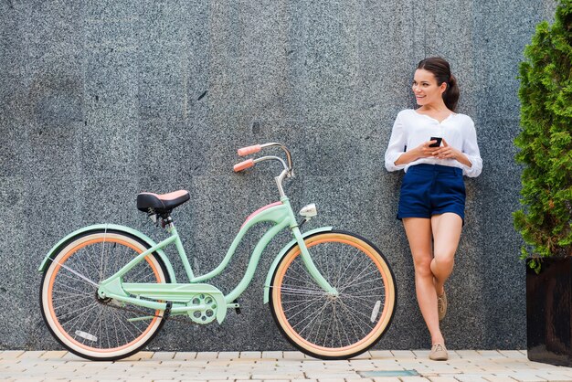 Jeune et élégant. Belle jeune femme souriante debout près de son vélo vintage dans la rue