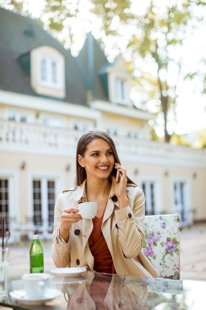 Jeune élégante belle femme assise dans le café de la ville, à l&#39;aide de téléphone portable et boit du café