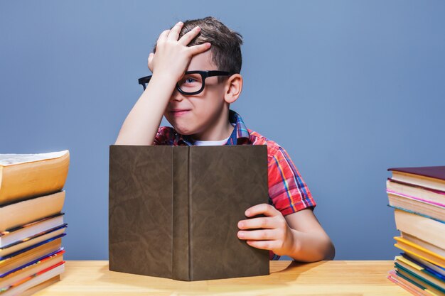 Jeune élève Dans Des Verres Avec Livre Assis Au Bureau De L'école. Obtenir Des Connaissances à Partir D'un Manuel