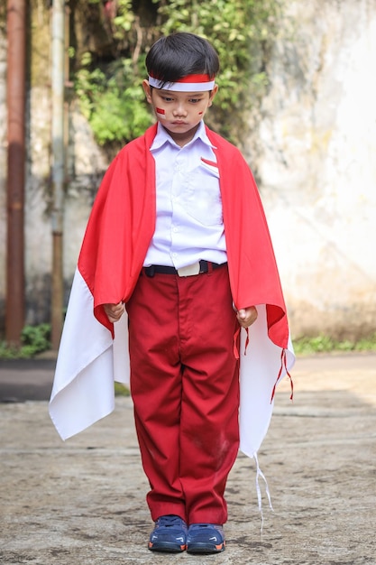 Un jeune élève de l'école primaire portant un uniforme et le drapeau indonésien regardant vers le bas