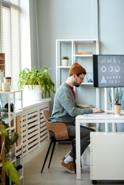 Jeune employé de bureau masculin sérieux assis sur le lieu de travail devant un ordinateur portable et se préparant pour le projet w