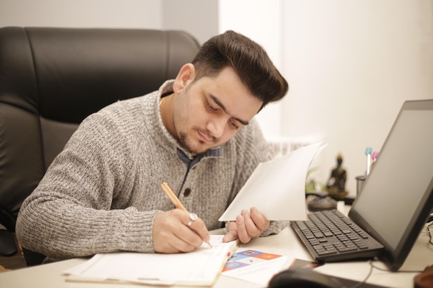 Un jeune employé écrit quelque chose dans un cahier avec un stylo.