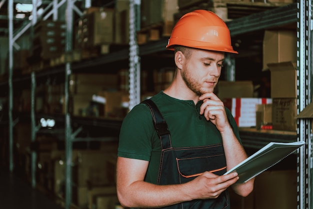 Jeune employé d&#39;entrepôt dans un casque avec un cahier