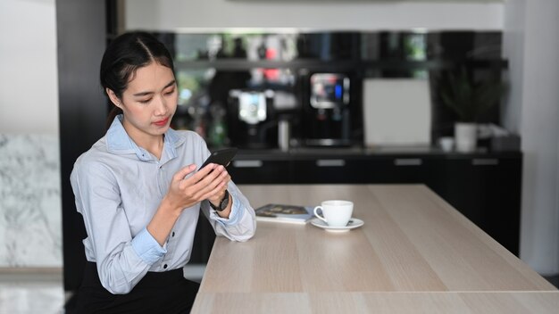 Jeune employée asiatique utilisant un téléphone portable pendant la pause-café au bureau.