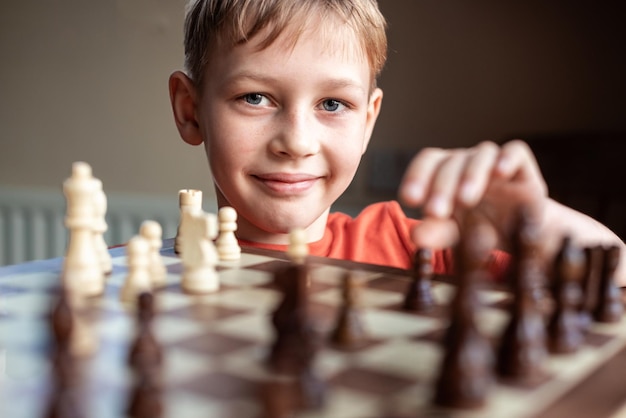 Jeune enfant blanc jouant une partie d'échecs sur un grand échiquier Échiquier sur table devant un écolier pensant au prochain coup