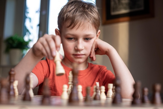 Jeune enfant blanc jouant une partie d'échecs sur un grand échiquier Échiquier sur table devant un écolier pensant au prochain coup