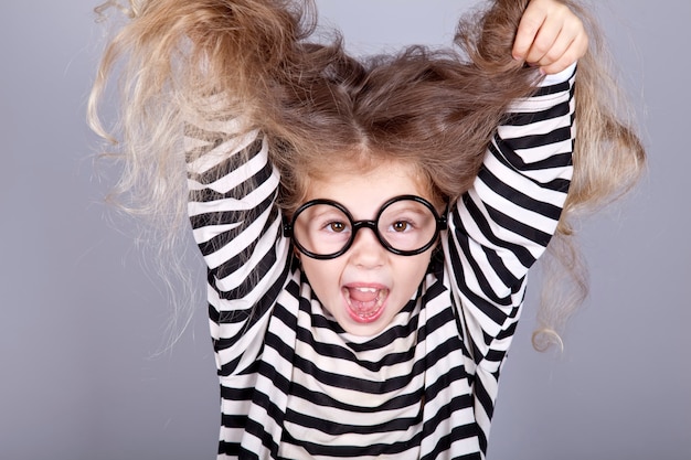 Jeune enfant criant à lunettes et veste en tricot rayé.