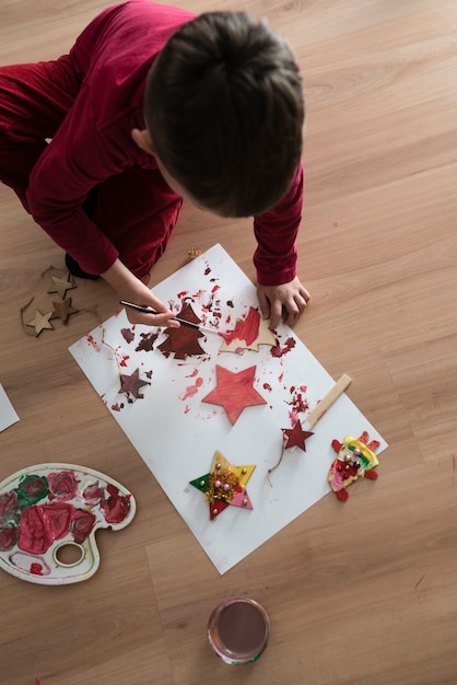 Jeune enfant faisant des décorations de Noël à genoux sur le sol dans une vue grand angle