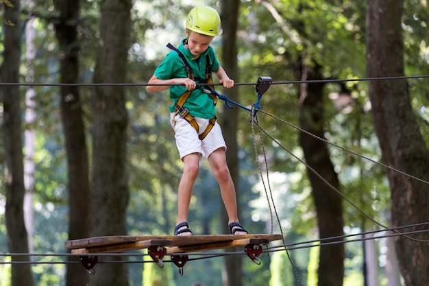 Jeune enfant garçon dans le harnais de sécurité et casque attaché avec une carabine à câble sur le chemin de la corde dans le parc.