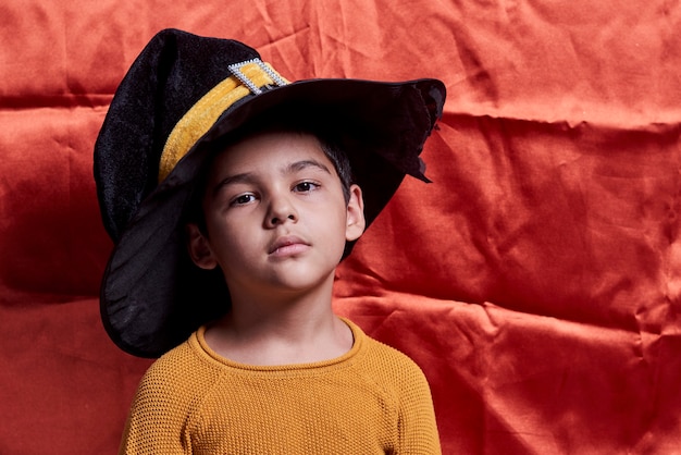 Un jeune enfant en pull orange portant un chapeau de sorcière portrait d'un garçon d'un an avec un grand hallowee noir...