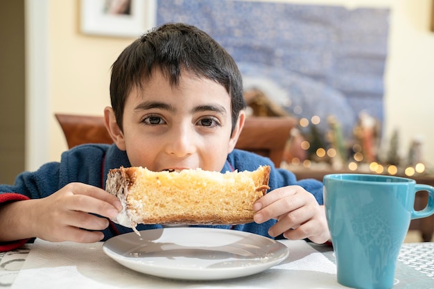 Le jeune enfant à la table le matin de noël prend le petit déjeuner avec pandoro