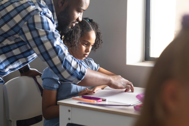 Jeune enseignant afro-américain enseignant une écolière élémentaire biraciale au bureau dans la salle de classe