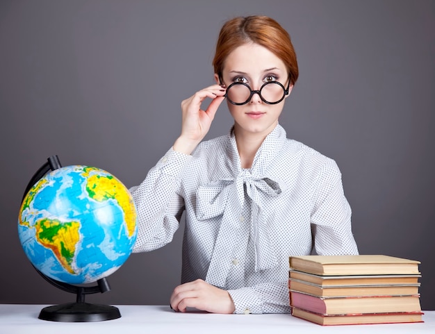 Le jeune enseignant dans des verres avec des livres et un globe.