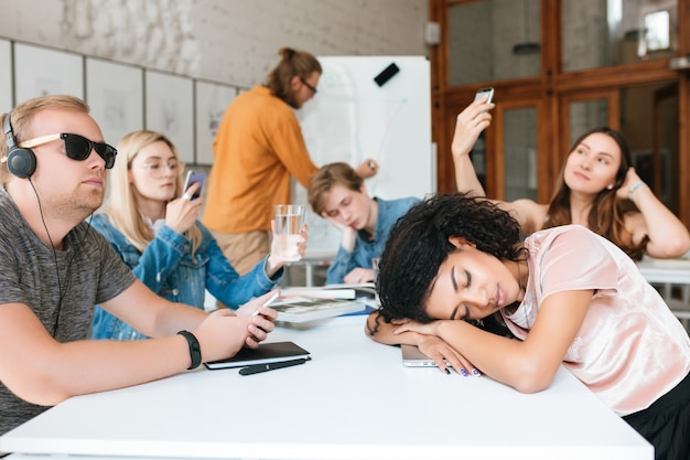 Jeune enseignant écrit à bord pendant que les élèves sont assis à la table et ne l'écoutent pas pendant la leçon