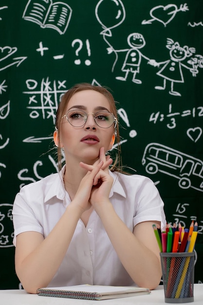 Jeune enseignant est assis près de tableau noir en classe