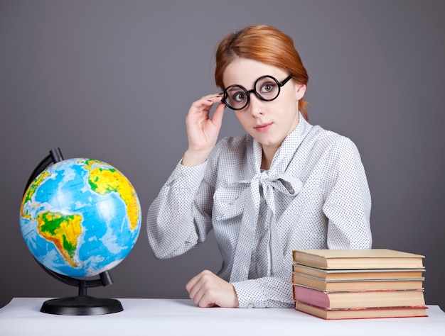 Le jeune enseignant à lunettes avec des livres et globe.