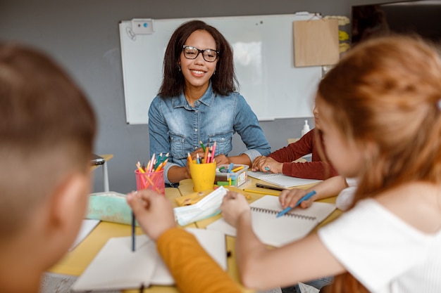 Jeune enseignant parlant avec des enfants pendant la leçon en classe