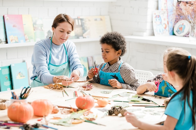 Jeune enseignant pointant sur bâton avec plusieurs décorations d'halloween liées à elle avec des fils tout en les montrant à un groupe de camarades de classe