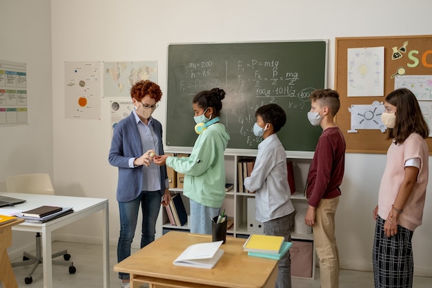 Jeune enseignant pulvérisant un désinfectant sur les mains des écoliers avant la leçon