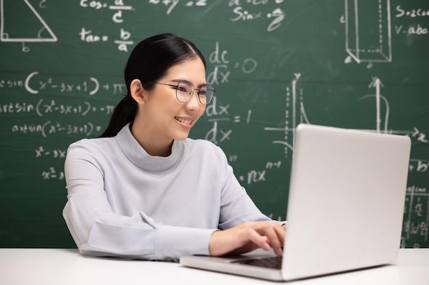Jeune enseignante asiatique assise à l'aide d'une vidéoconférence sur ordinateur portable avec une étudiante Enseignante formant les mathématiques en classe à partir d'un flux en direct avec un cours en ligne sur ordinateur