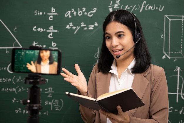 Jeune enseignante asiatique femme debout regardant la caméra et la vidéoconférence avec une étudiante Enseignante formant les mathématiques en classe à partir d'un flux en direct avec un cours en ligne pour smartphone