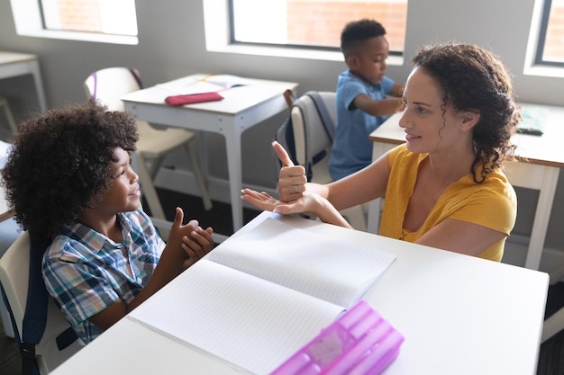 Une jeune enseignante blanche enseigne le langage des signes à un élémentaire afro-américain en classe.