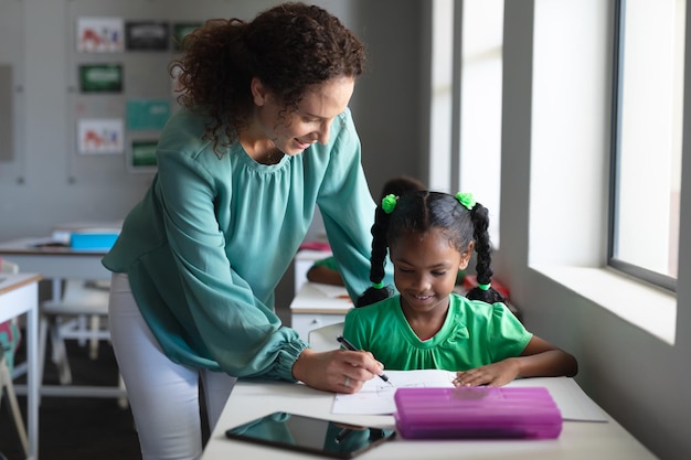 Photo une jeune enseignante caucasienne aide une écolière afro-américaine à écrire sur un livre.