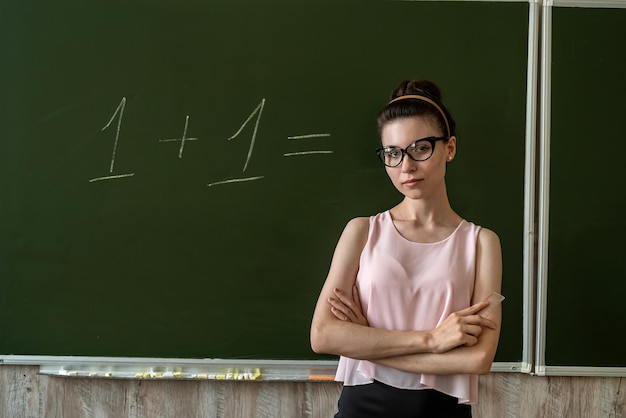 jeune enseignante du primaire écrit sur le tableau un plus un, concept d'éducation