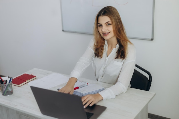 Une jeune enseignante travaille à l'ordinateur Elle porte une chemise blanche Organise une formation en ligne pour les étudiants Cours en ligne Webinaire