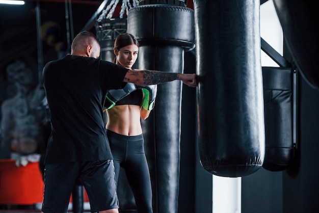 Un jeune entraîneur de boxe tatoué enseigne à une jeune femme au gymnase.
